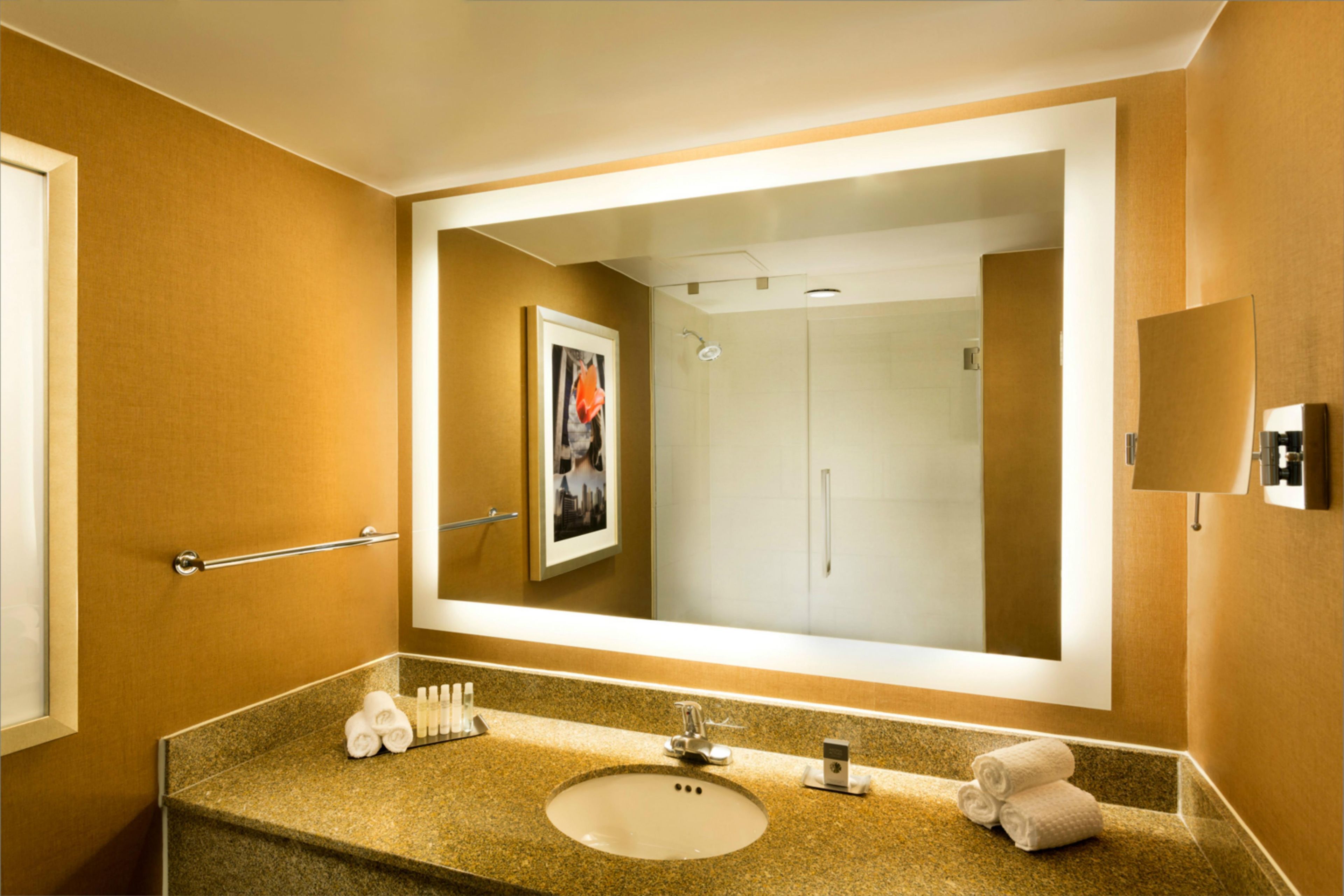 A hotel bathroom with a large mirror, a sink, and a shower.