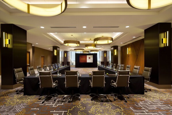 A conference room with a long table, multiple chairs, and a stage with a podium.
