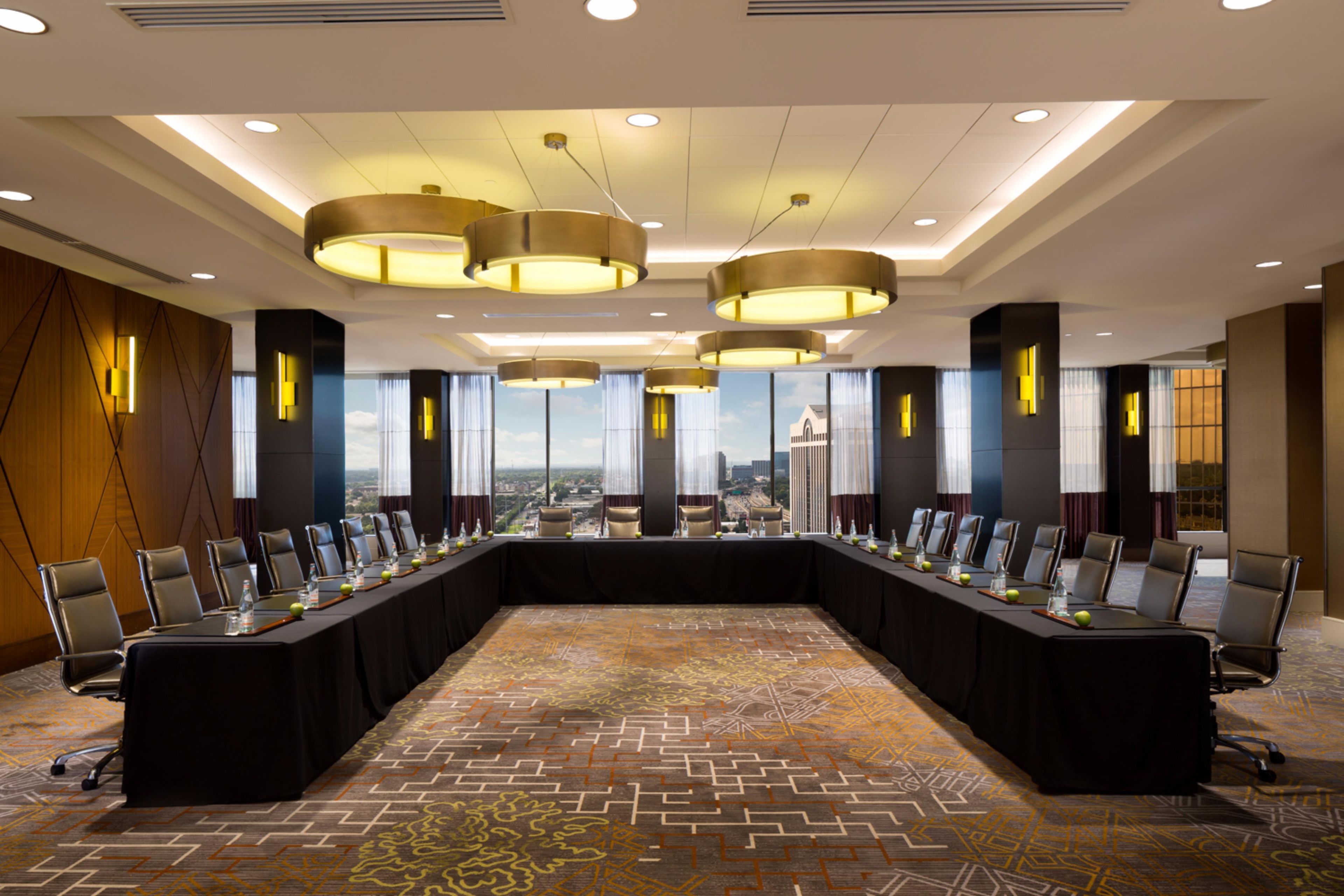 A conference room with a long table, multiple chairs, and a city view through large windows.
