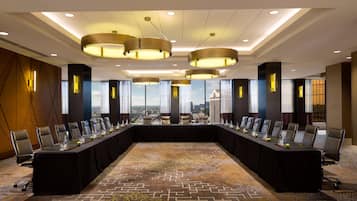 A conference room with a long table, multiple chairs, and a city view through large windows.