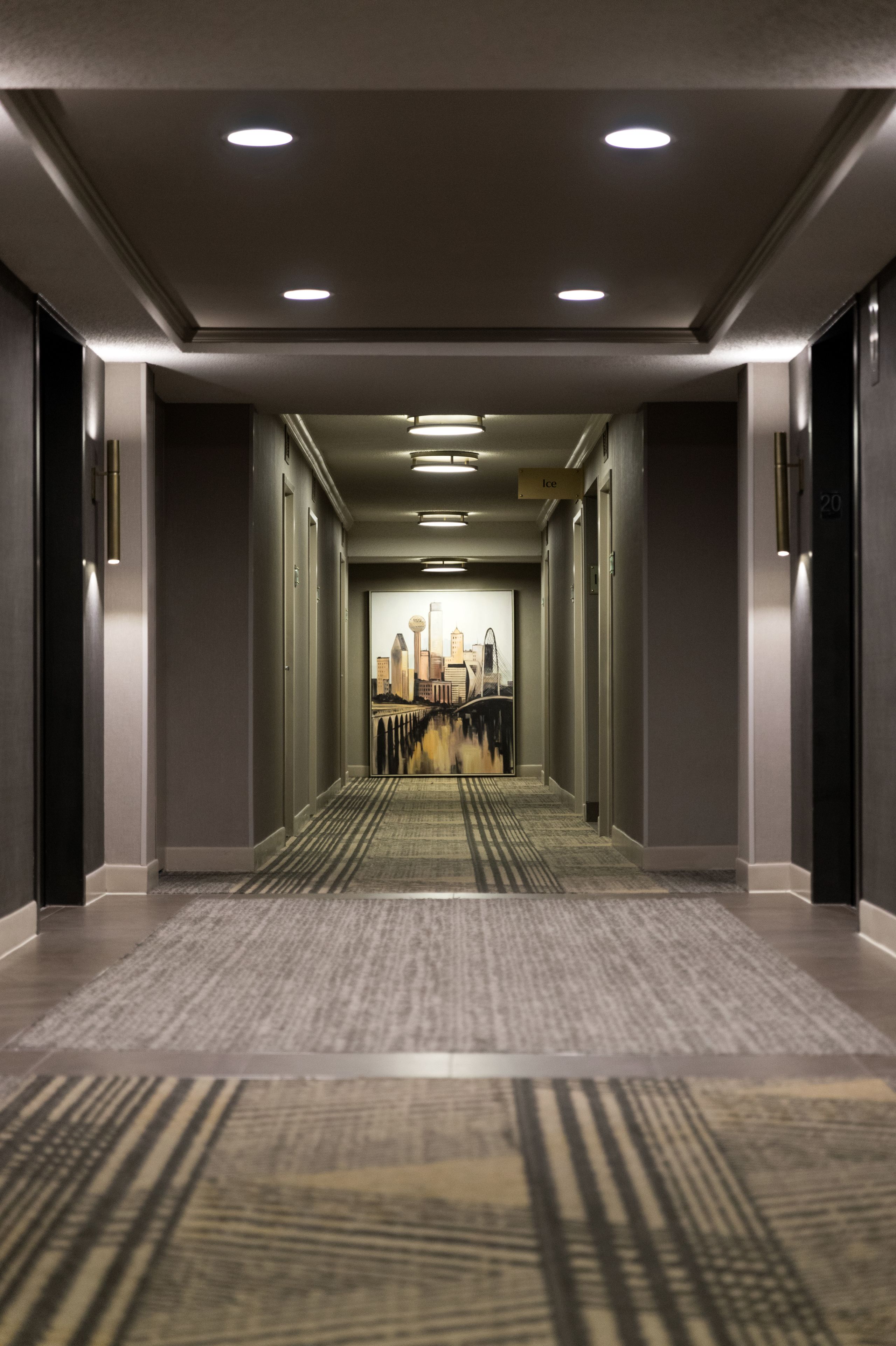 Un pasillo de hotel con piso alfombrado, iluminación empotrada y un mural con vistas a la ciudad.
