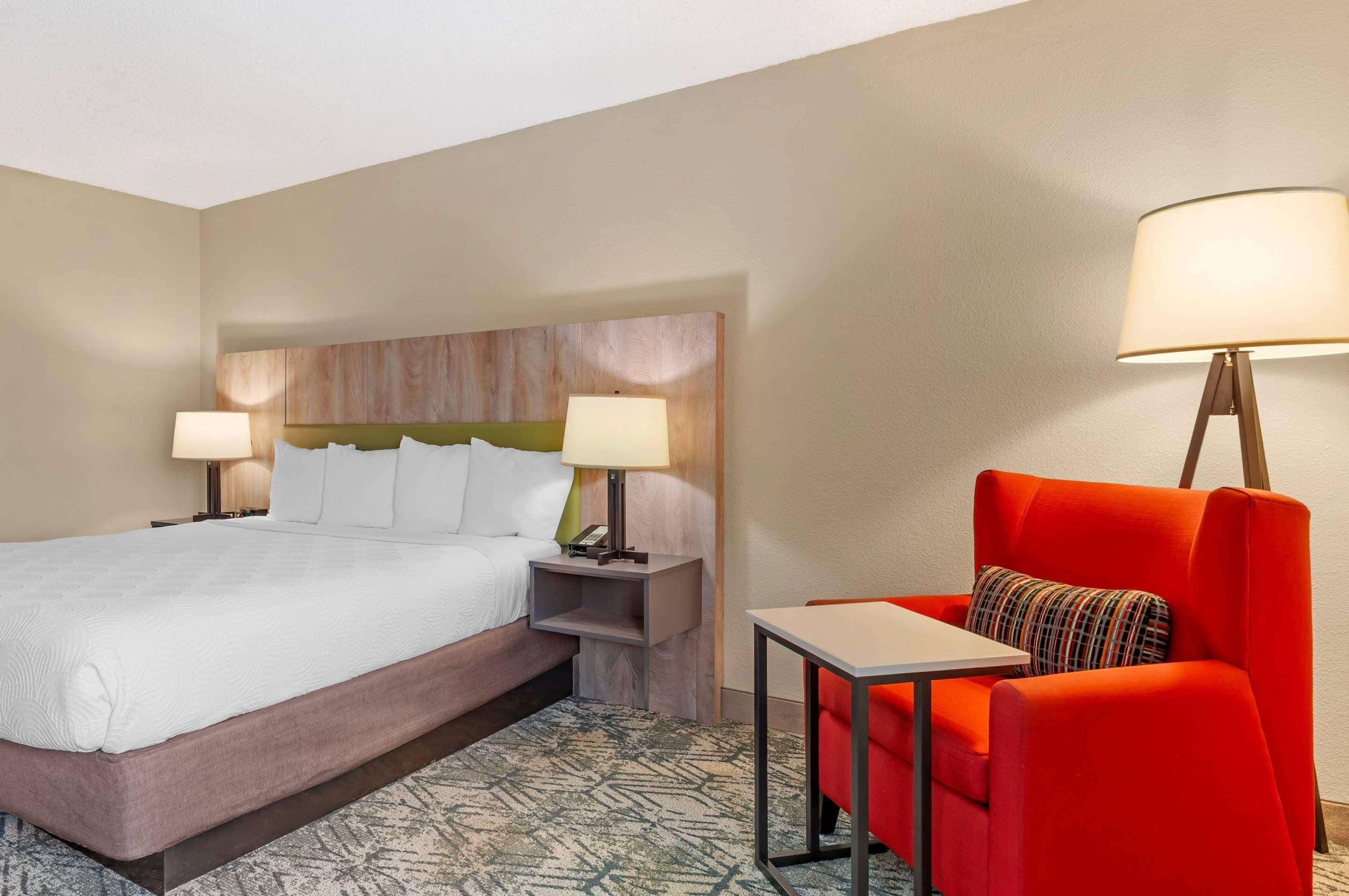 A hotel room with a bed, bedside tables, a desk, a chair, and a lamp.