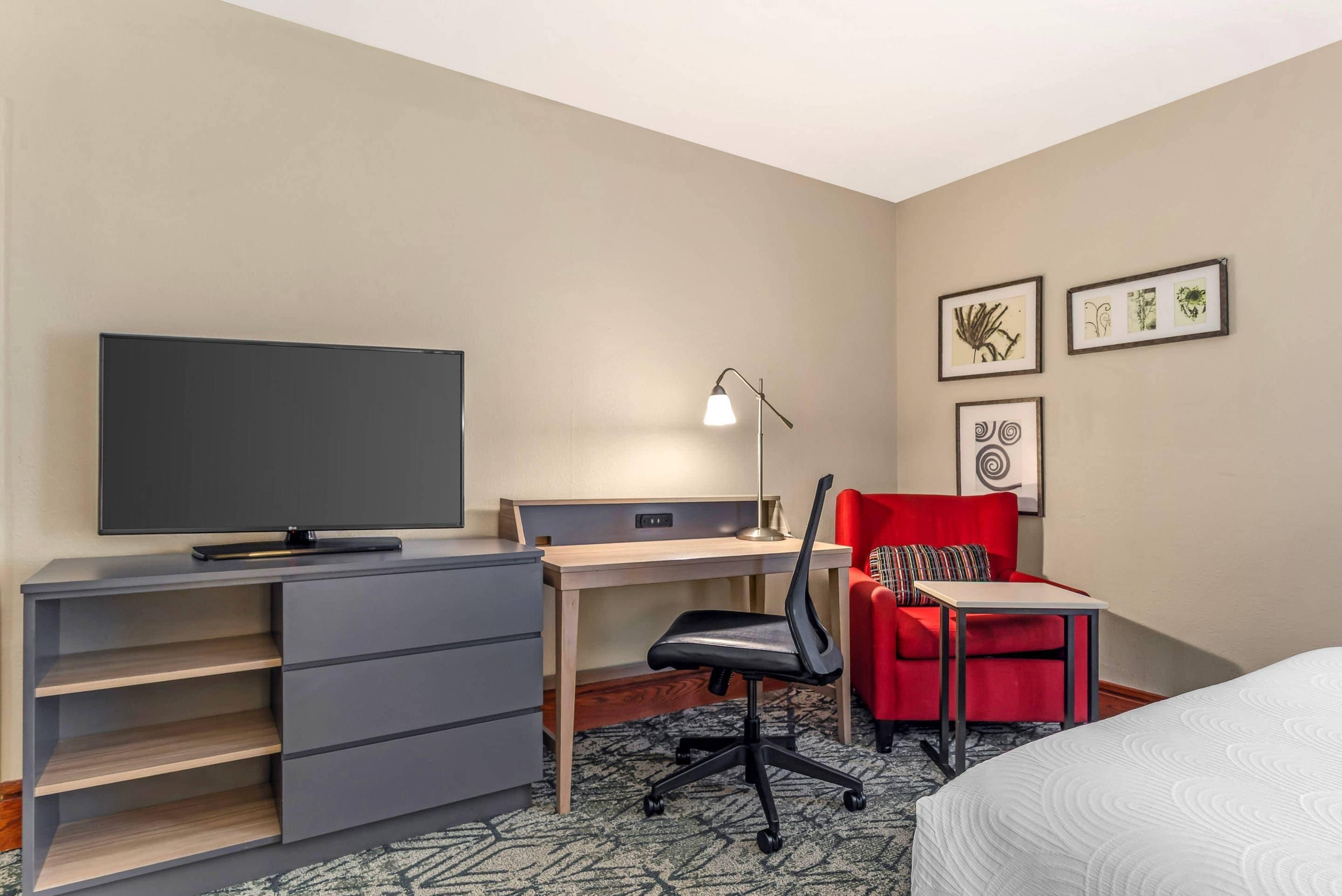 A hotel room with a bed, a desk, a chair, a TV, and a lamp.