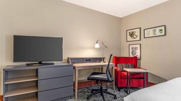 A hotel room with a bed, a desk, a chair, a TV, and a lamp.