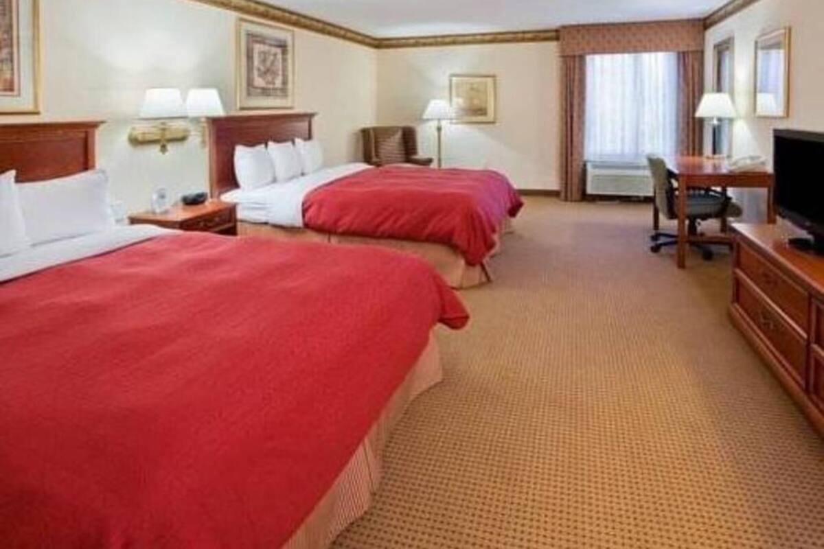 A hotel room with two beds, a desk, a chair, a television, and a window with curtains.