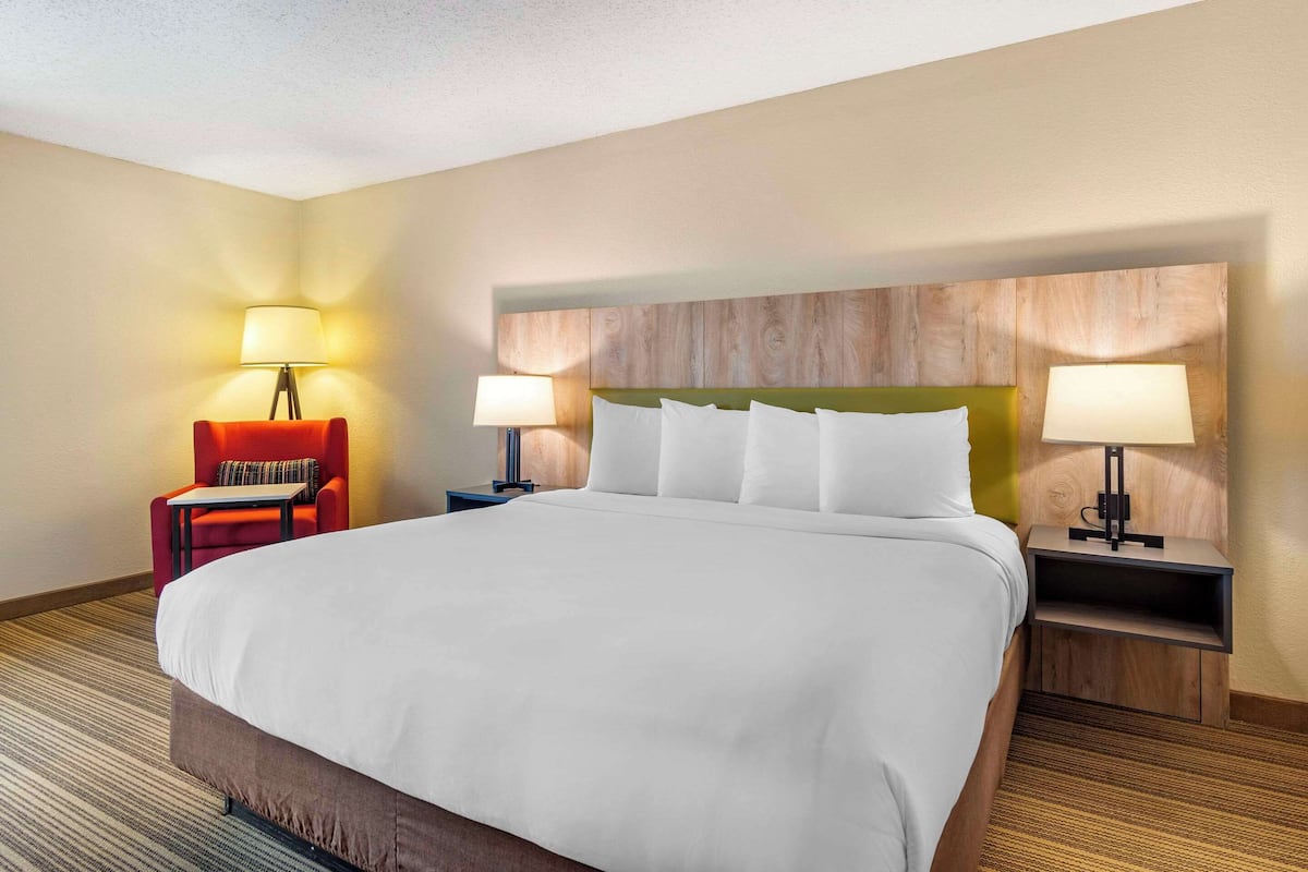 A hotel room with a large bed, two bedside tables with lamps, a red armchair, and a small table.