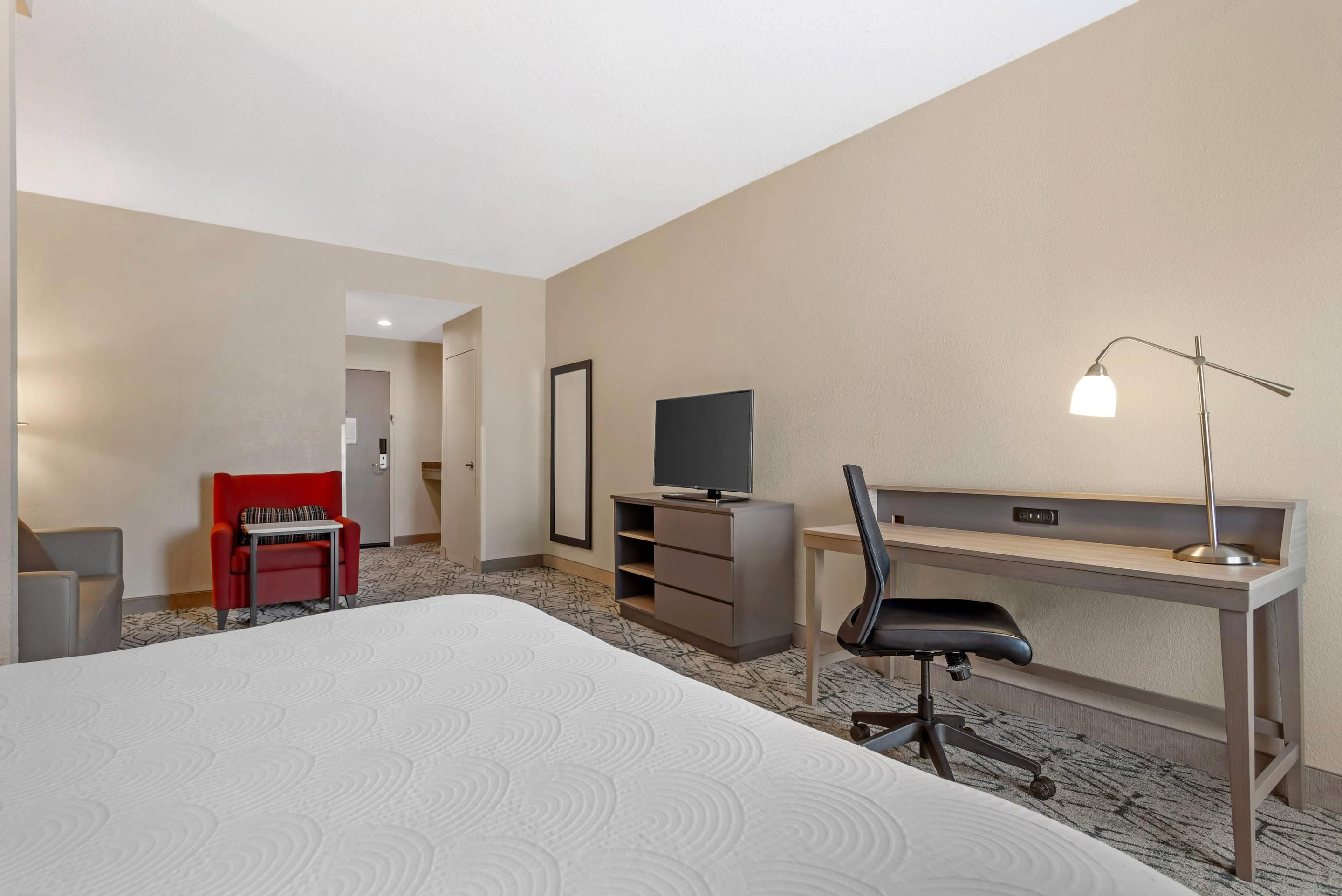 A hotel room with a bed, a desk, a chair, a television, and a lamp.
