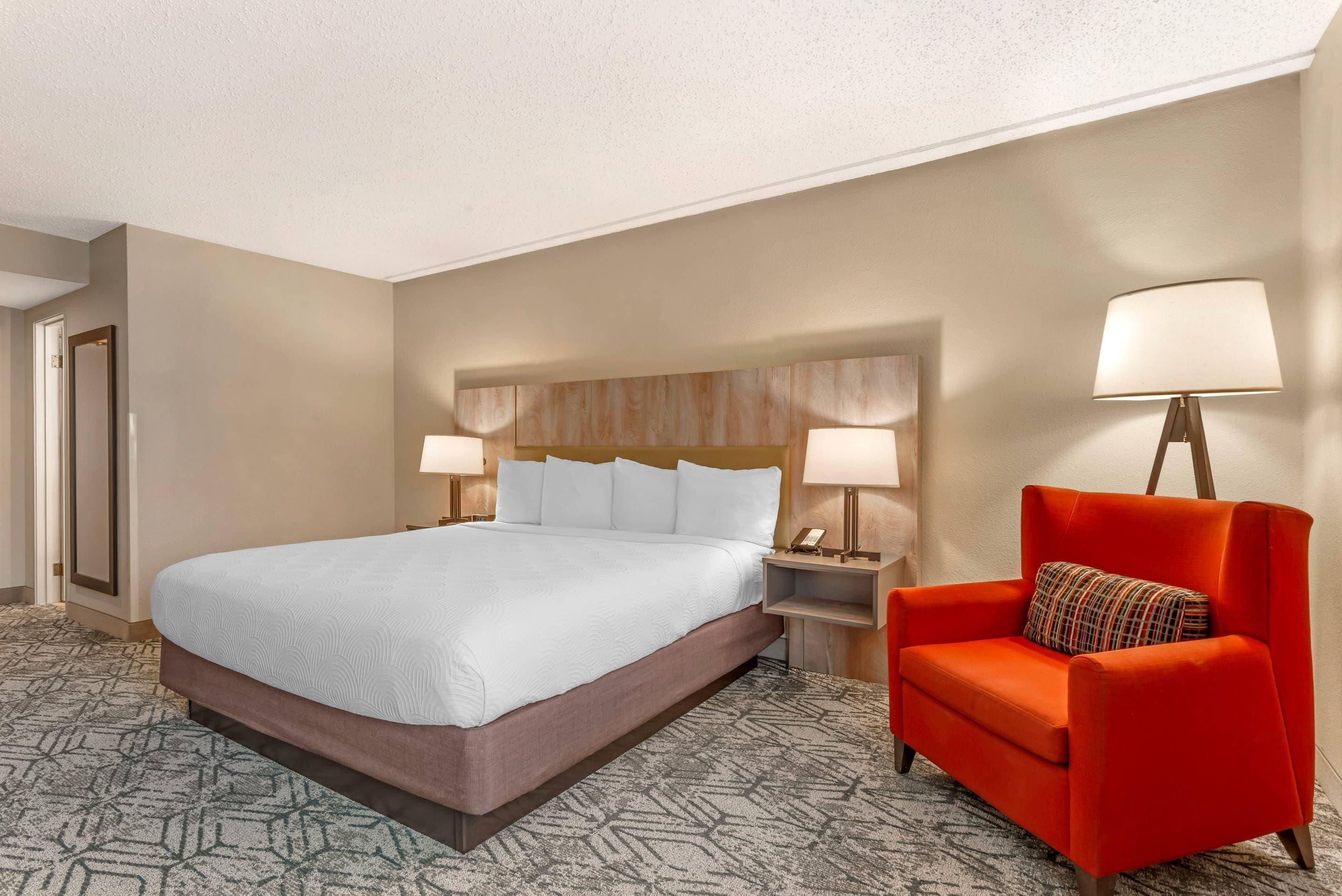 A hotel room with a large bed, two bedside lamps, a red armchair, and a patterned carpet.