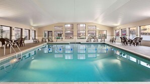 An indoor swimming pool with clear water, surrounded by lounge chairs and tables, with large windows offering views of the outside. - Country Inn & Suites by Radisson, Atlanta Galleria/Ballpark, GA (Atlanta)