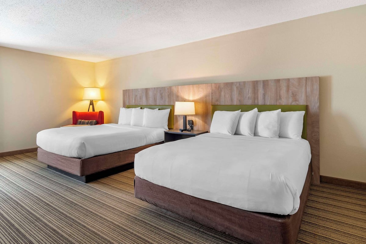 A hotel room with two beds, each with a wooden headboard, a nightstand, and a lamp.
