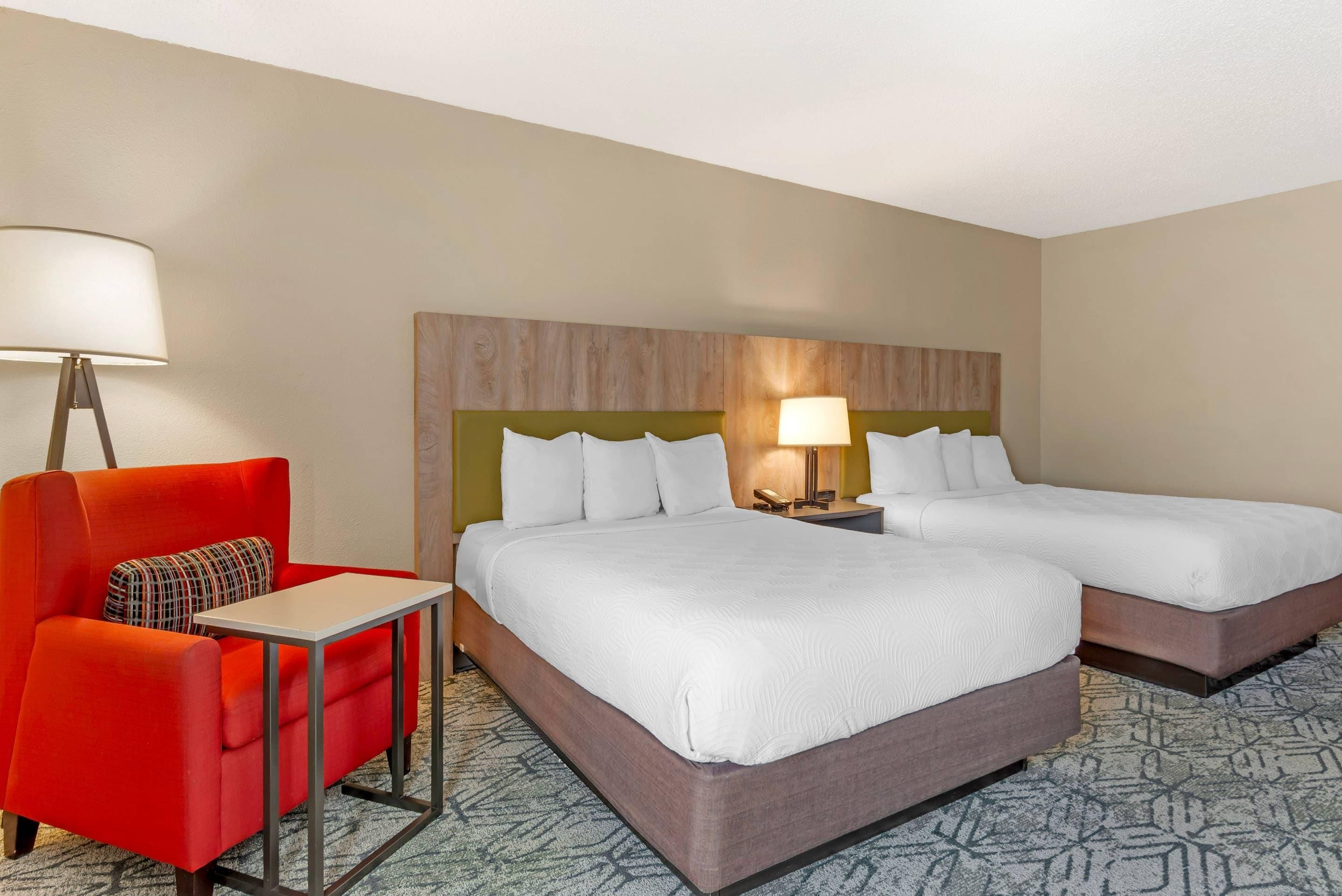 A hotel room with a bed, bedside tables, a desk, a chair, and a lamp.