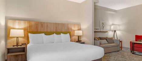 A hotel room with a large bed, two bedside tables with lamps, a sofa, a red chair, and a floor lamp.