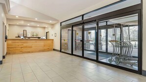 A hotel reception area with a wooden reception desk, framed pictures, and a view of the parking area through glass doors. - Country Inn & Suites by Radisson, Atlanta Galleria/Ballpark, GA (Atlanta)