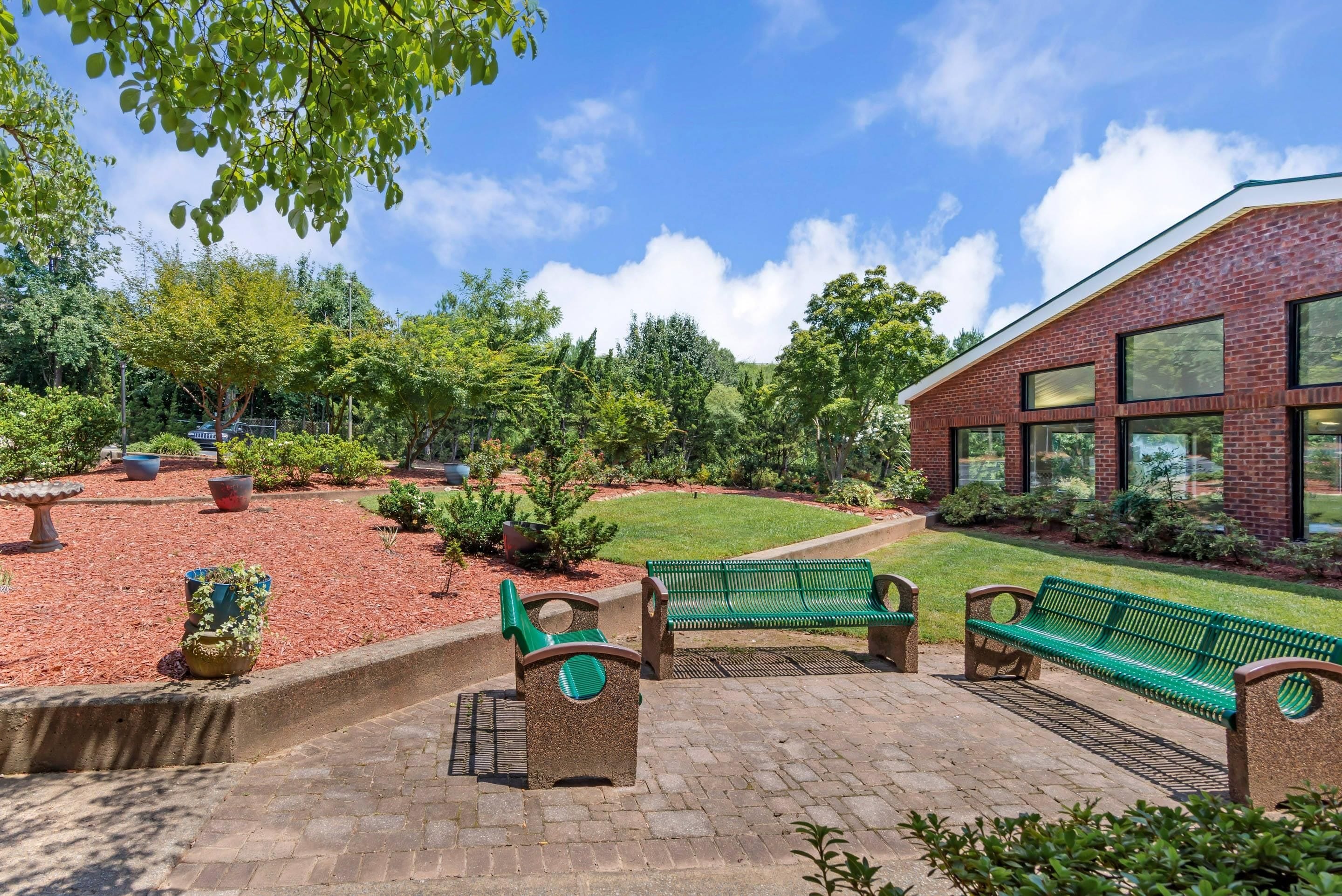 En anlagt have med en murstensbygning, grønne bænke og mange forskellige planter.