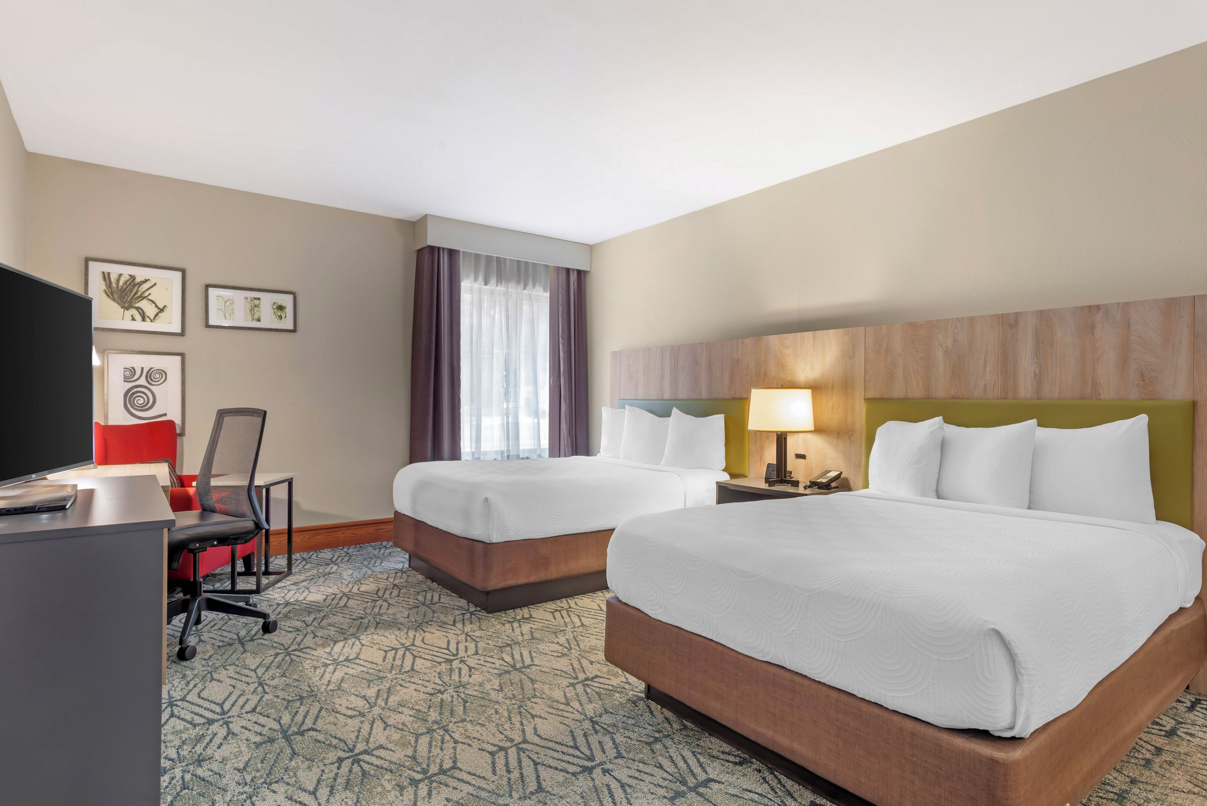 A hotel room with two beds, a desk with a computer, a chair, and a television.