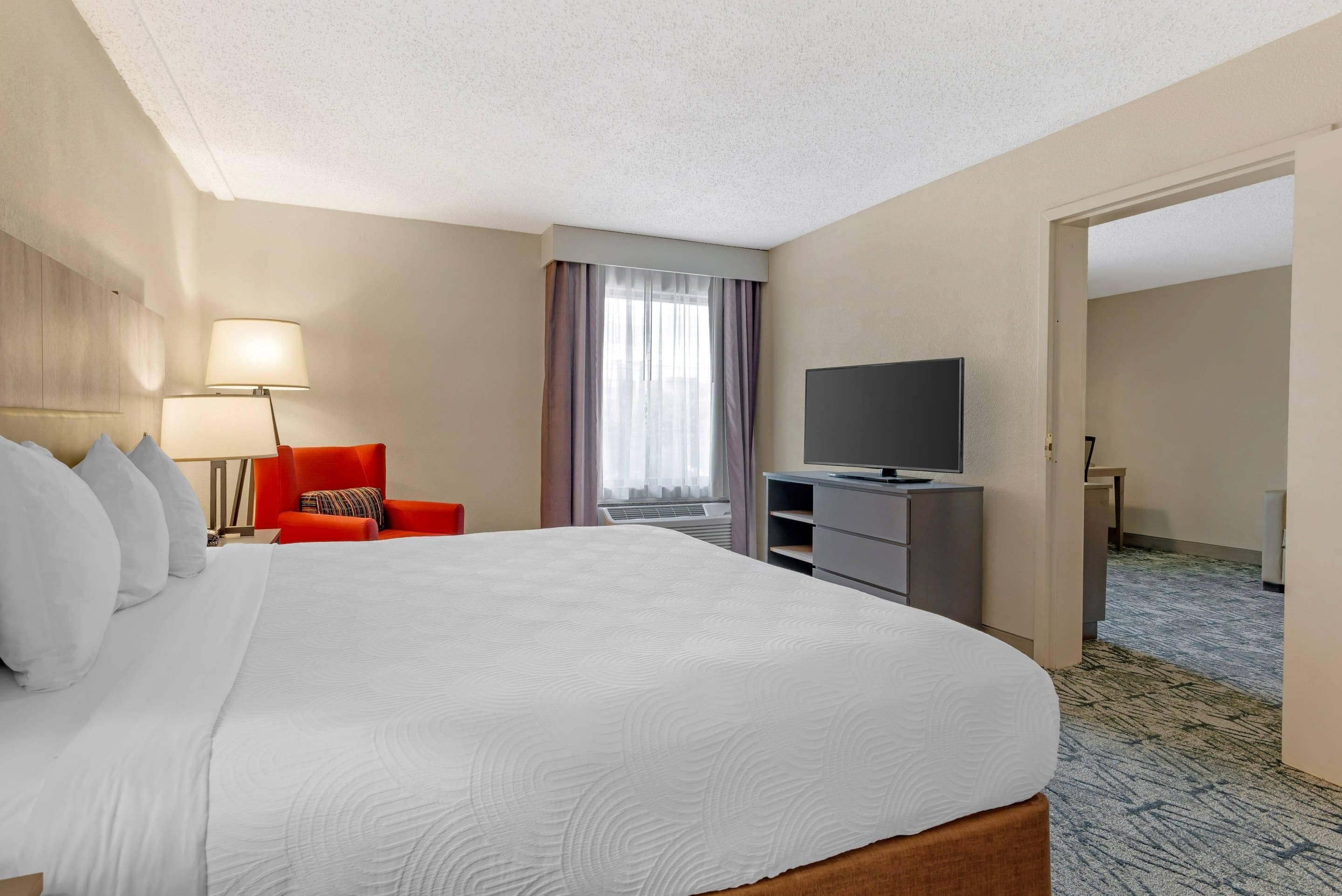 Une chambre d’hôtel avec un grand lit, un fauteuil rouge, une télévision et un bureau.