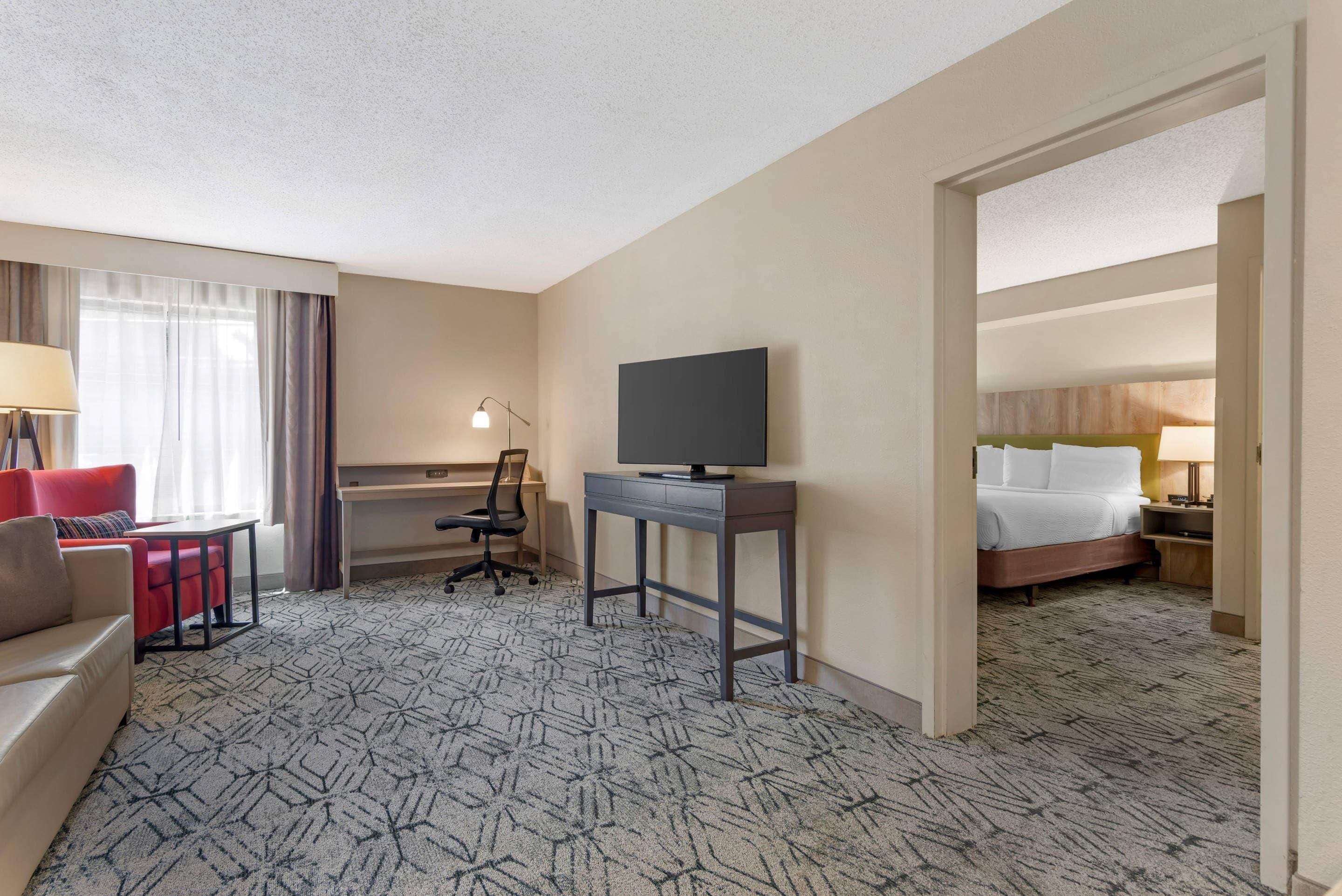A hotel room with a bed, a desk, a chair, a television, and a sofa.