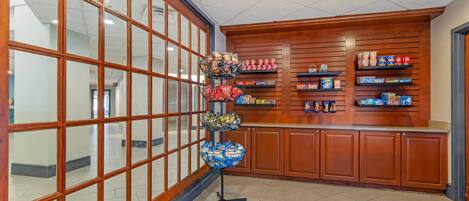 Interior de una tienda con una exhibición de aperitivos y bebidas en estantes, un mostrador con bolsas de papas, y un amplio ventanal con vistas al exterior.
