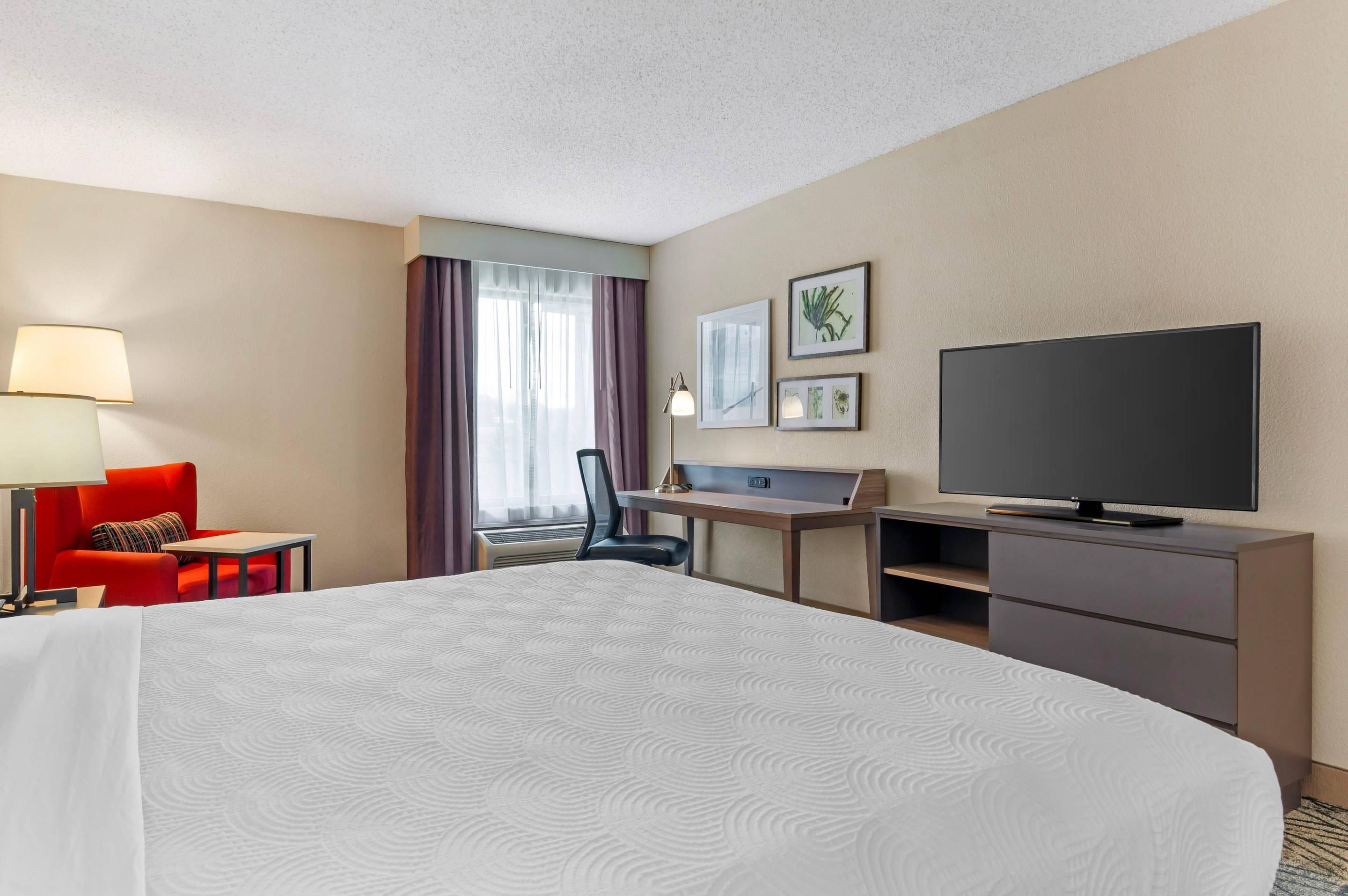A hotel room with a large bed, a desk with a chair, a television, and a window with curtains.