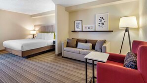 A hotel room with a bed, a sofa, a red armchair, a small table, and wall-mounted artwork. - Country Inn & Suites by Radisson, Atlanta Galleria/Ballpark, GA (Atlanta)