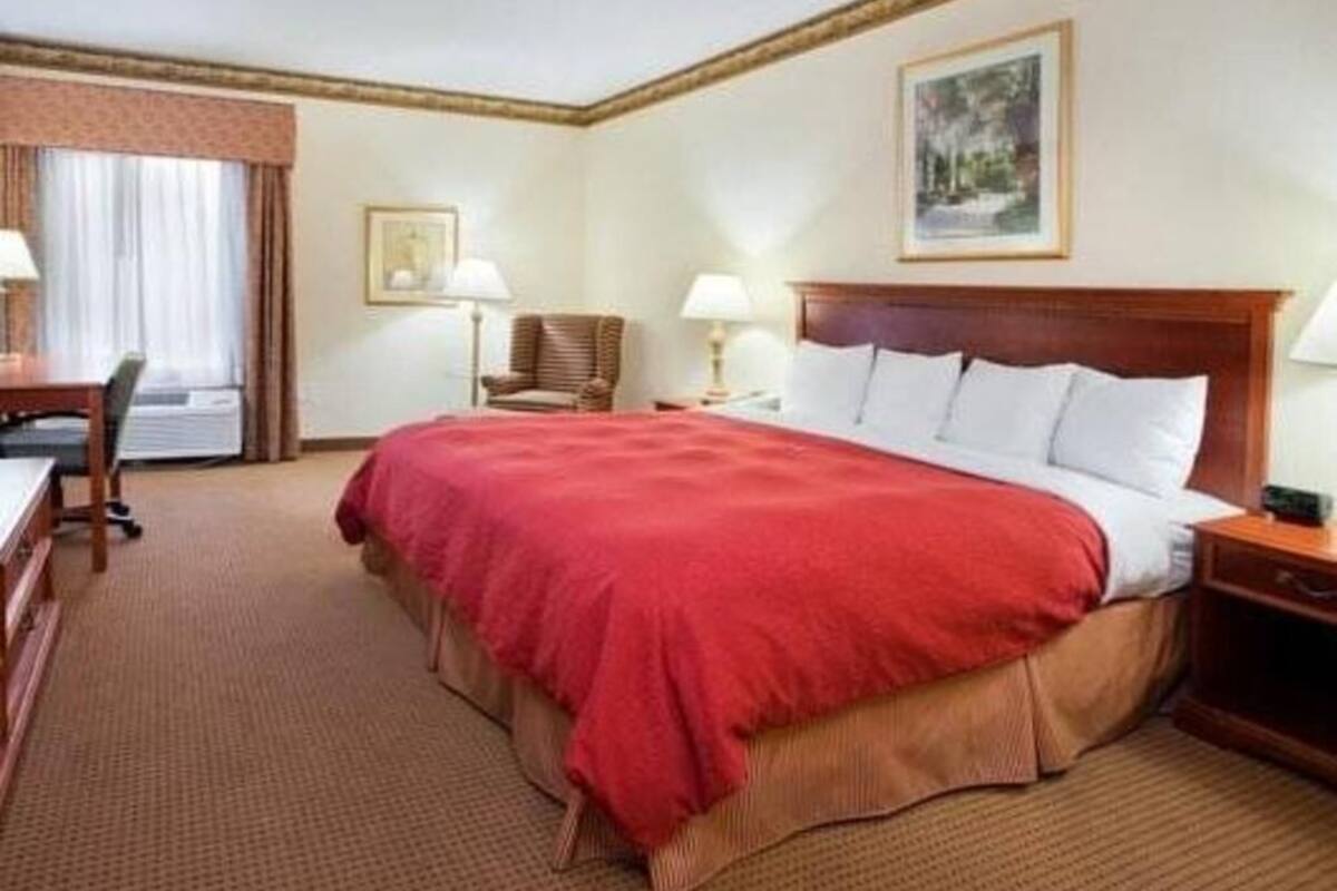 A hotel room with a large bed, a desk, a chair, and a nightstand.
