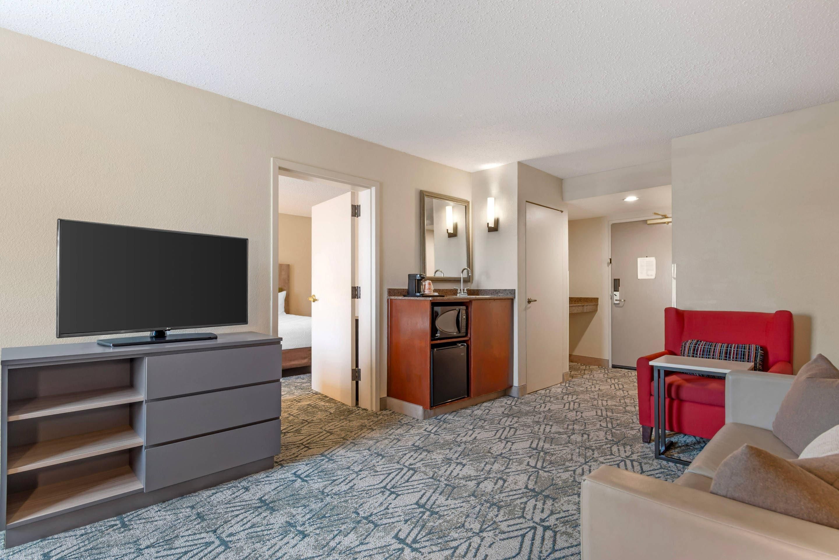 Habitación de hotel con televisión, kitchenette, un sillón rojo y cama.