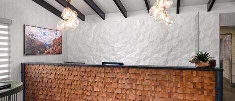 A reception desk with a wooden block design, a modern chandelier, and a textured white wall.