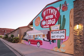 A mural advertising a motor lodge with a swim pool, a vintage car, and a cactus.