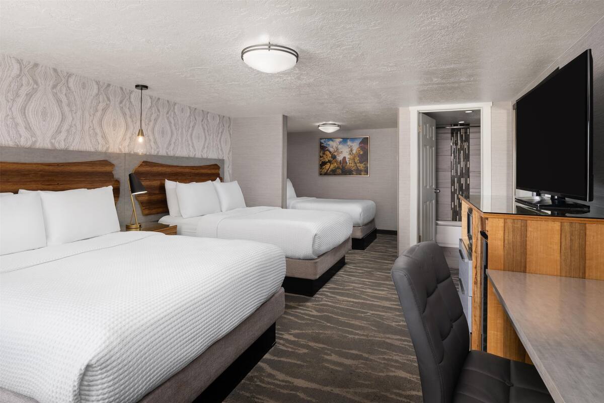 A hotel room with two beds, a desk, a TV, and a shower area.