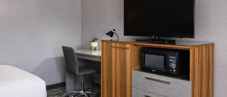 A hotel room with a bed, a desk with a computer, a television, and a microwave.