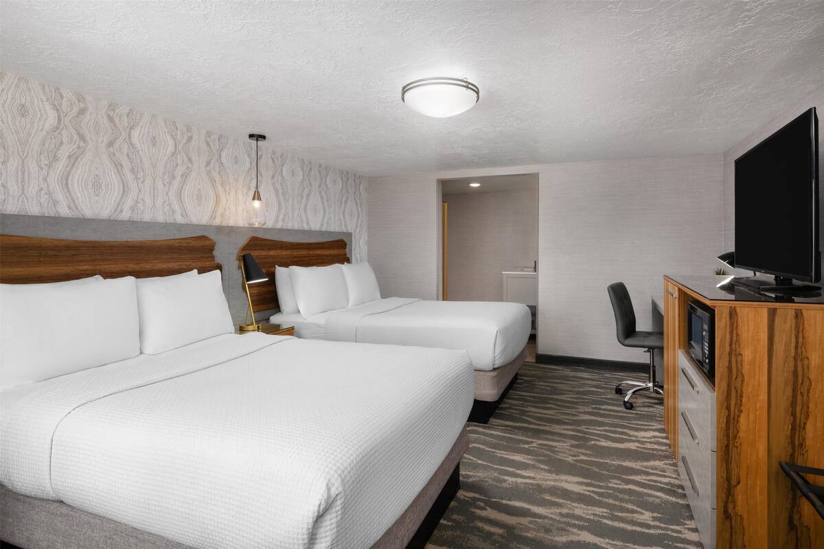 A hotel room with two beds, a desk with a TV, and a patterned carpet.