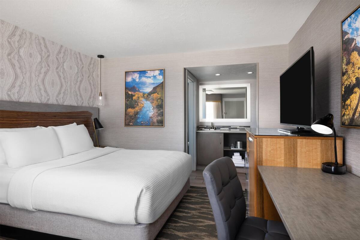 A hotel room with a large bed, a desk with a computer, a TV, and a painting on the wall.