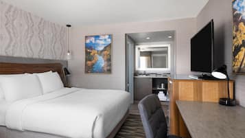 A hotel room with a large bed, a desk with a computer, a TV, and a painting on the wall.
