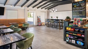 Un café moderne doté d’un bar, de différents espaces pour s’asseoir et d’un tableau affichant le menu.
