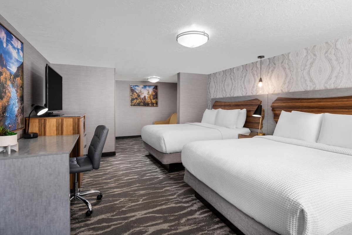 A hotel room with two beds, a desk with a computer, a chair, and a television.