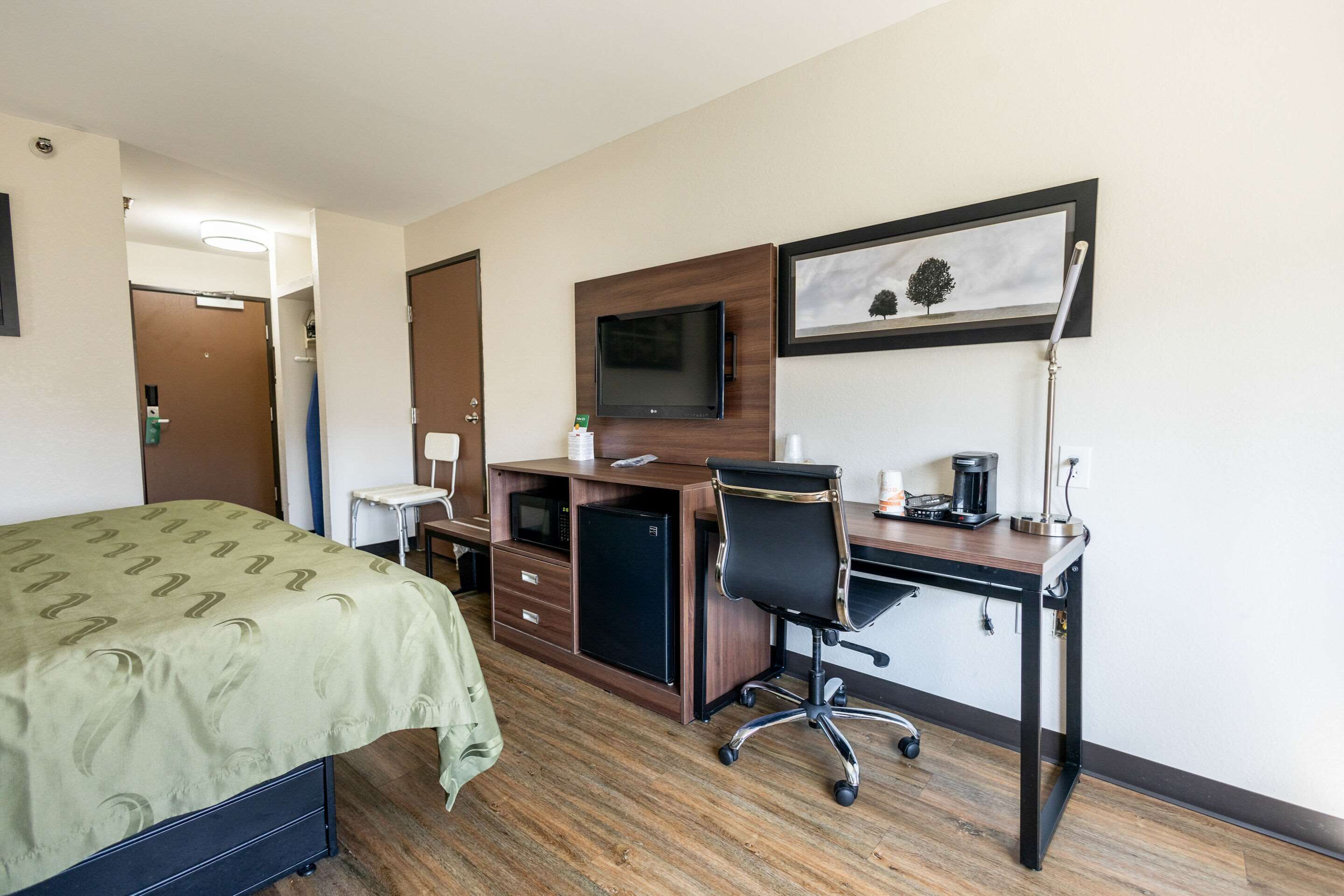 Habitación de hotel con cama, escritorio, computadora, televisor y cafetera.