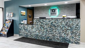 Zona de recepción de un hotel con diseño moderno, que incluye una pared de mosaicos, un mostrador de recepción y una pantalla digital.