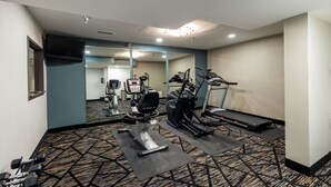 Un gimnasio hotelero con máquinas de cardio, pesas libres y un espejo.