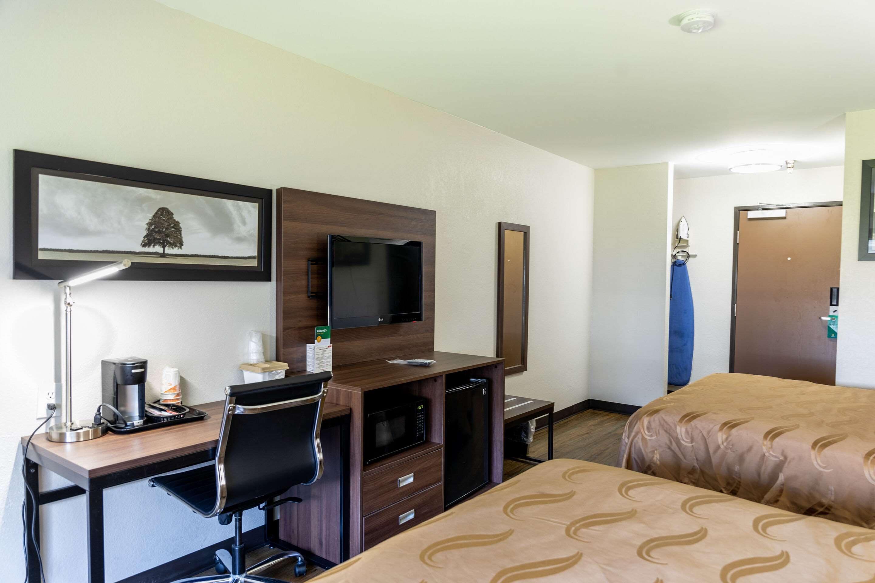 A hotel room with a desk, a television, a bed with patterned bedding, a coffee maker, and a mirror.