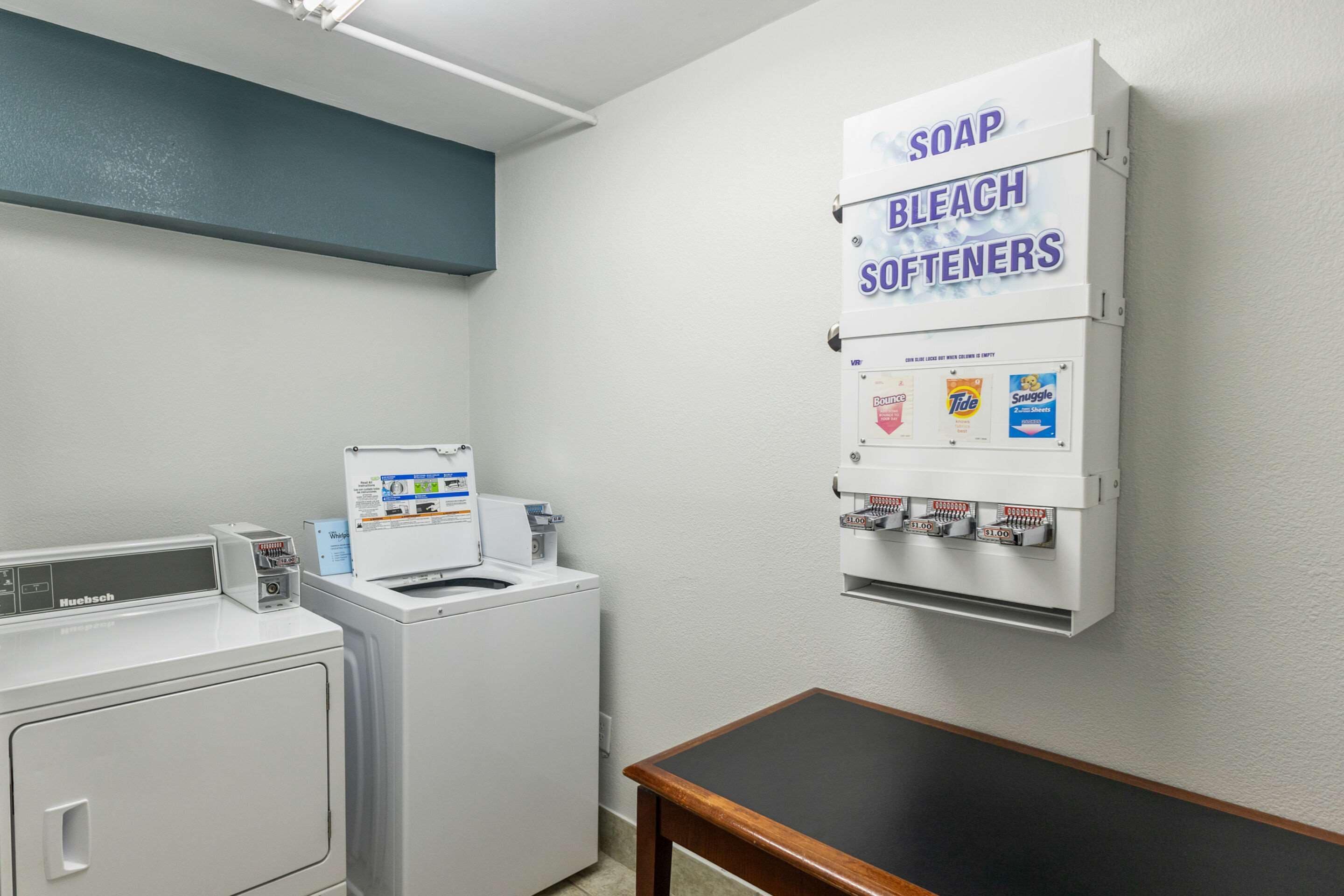 Een wasserette met een wasmachine, droger en een wanddispenser voor zeep, bleekmiddel en wasverzachter.