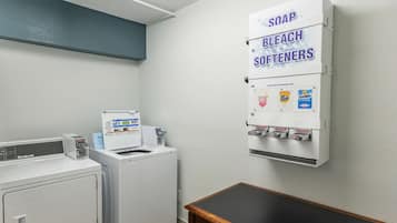 Een wasserette met een wasmachine, droger en een wanddispenser voor zeep, bleekmiddel en wasverzachter.