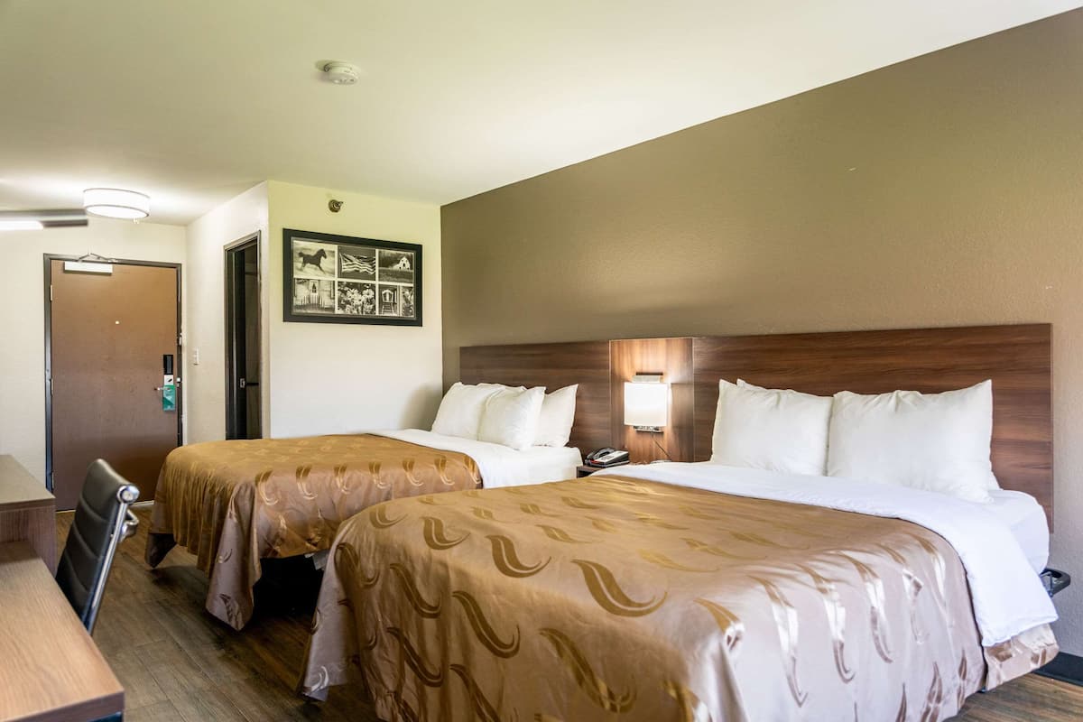 A hotel room with two beds, a desk, and a door.