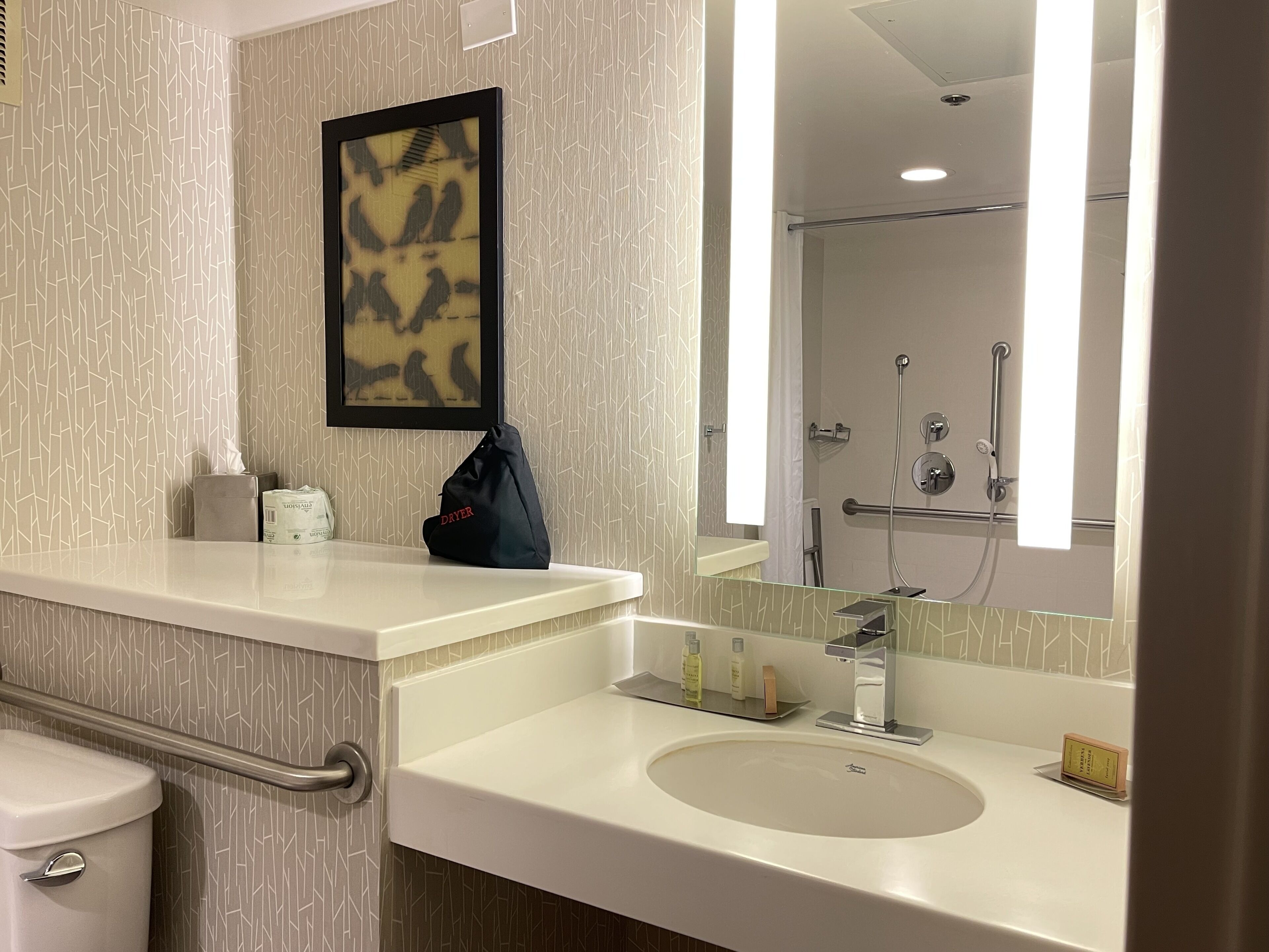 A modern bathroom with a white sink, a mirror, and a shower area.