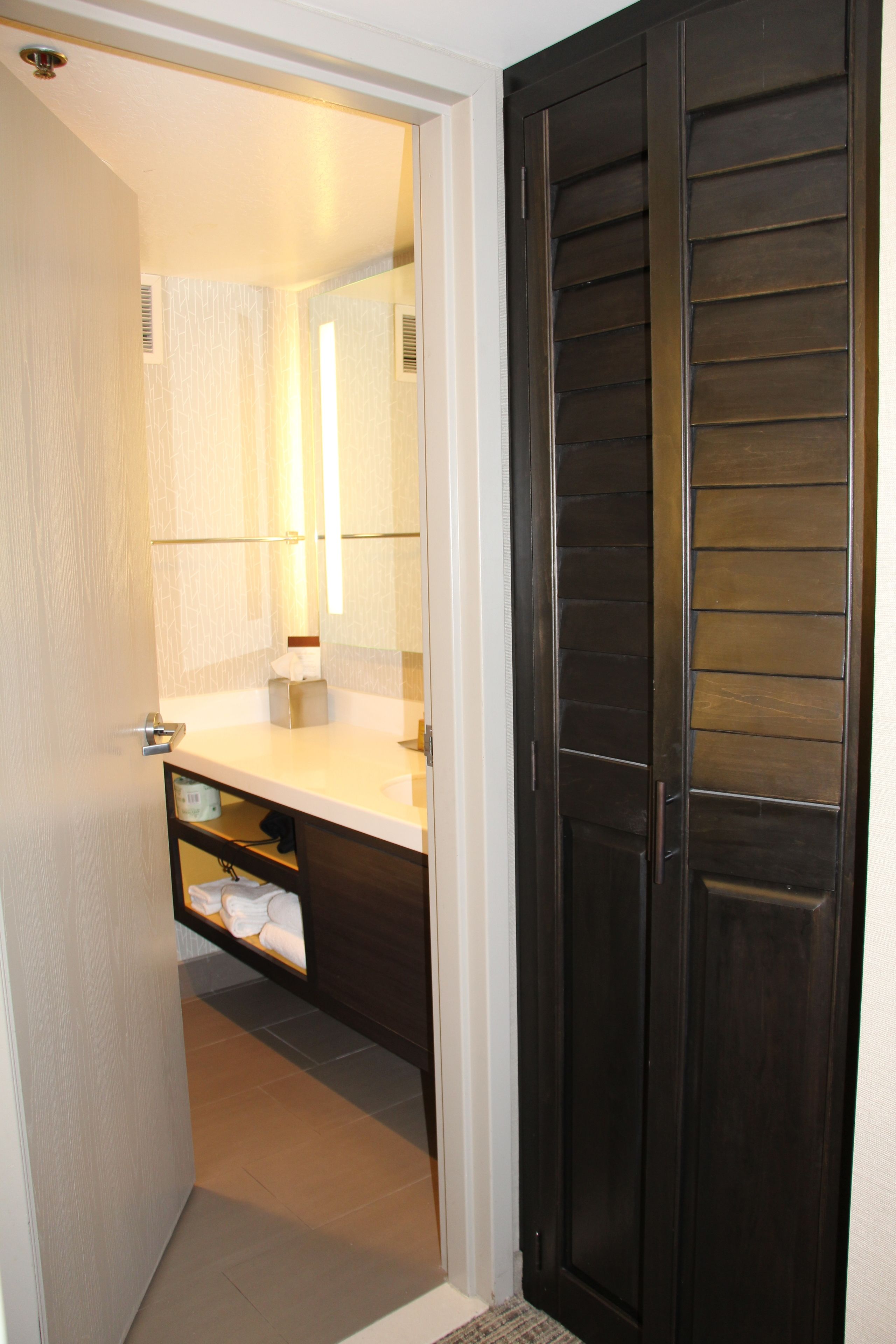 Un baño con una puerta de madera oscura, un lavamanos blanco y un perchero para toallas.