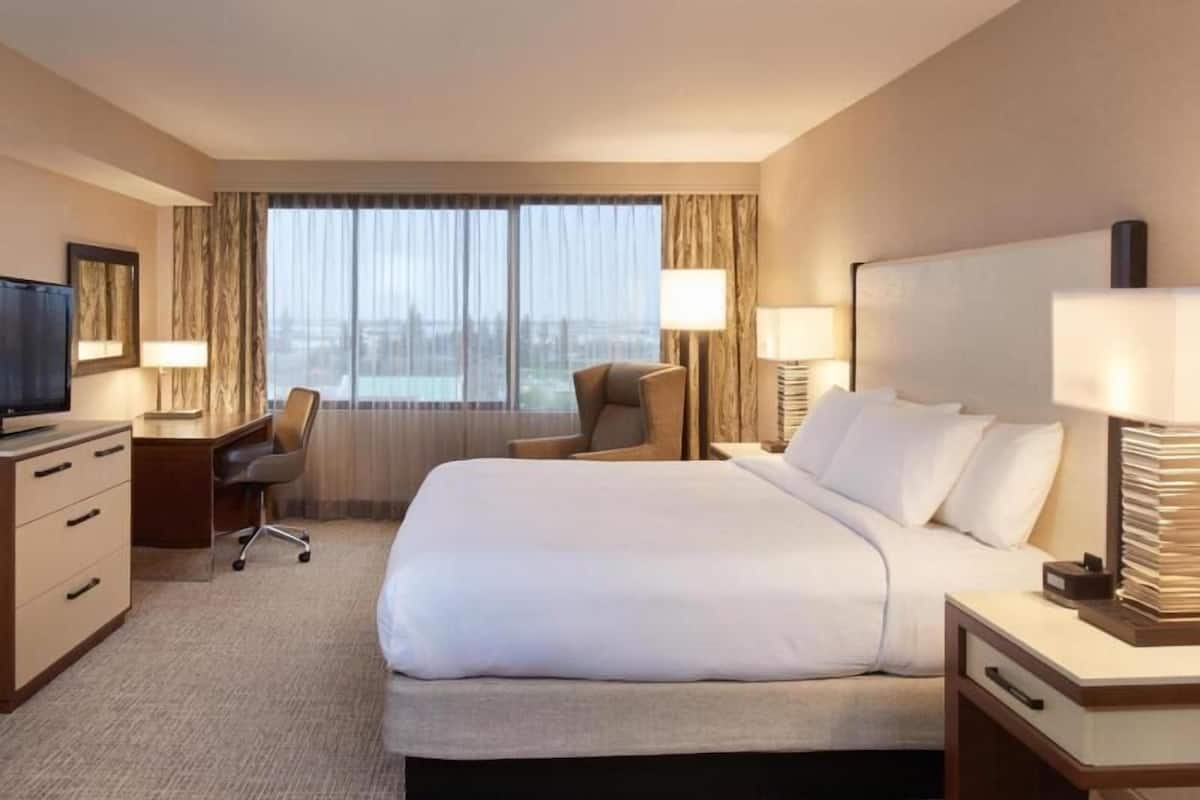 A hotel room with a large bed, a desk with a chair, a television, and a window with curtains.
