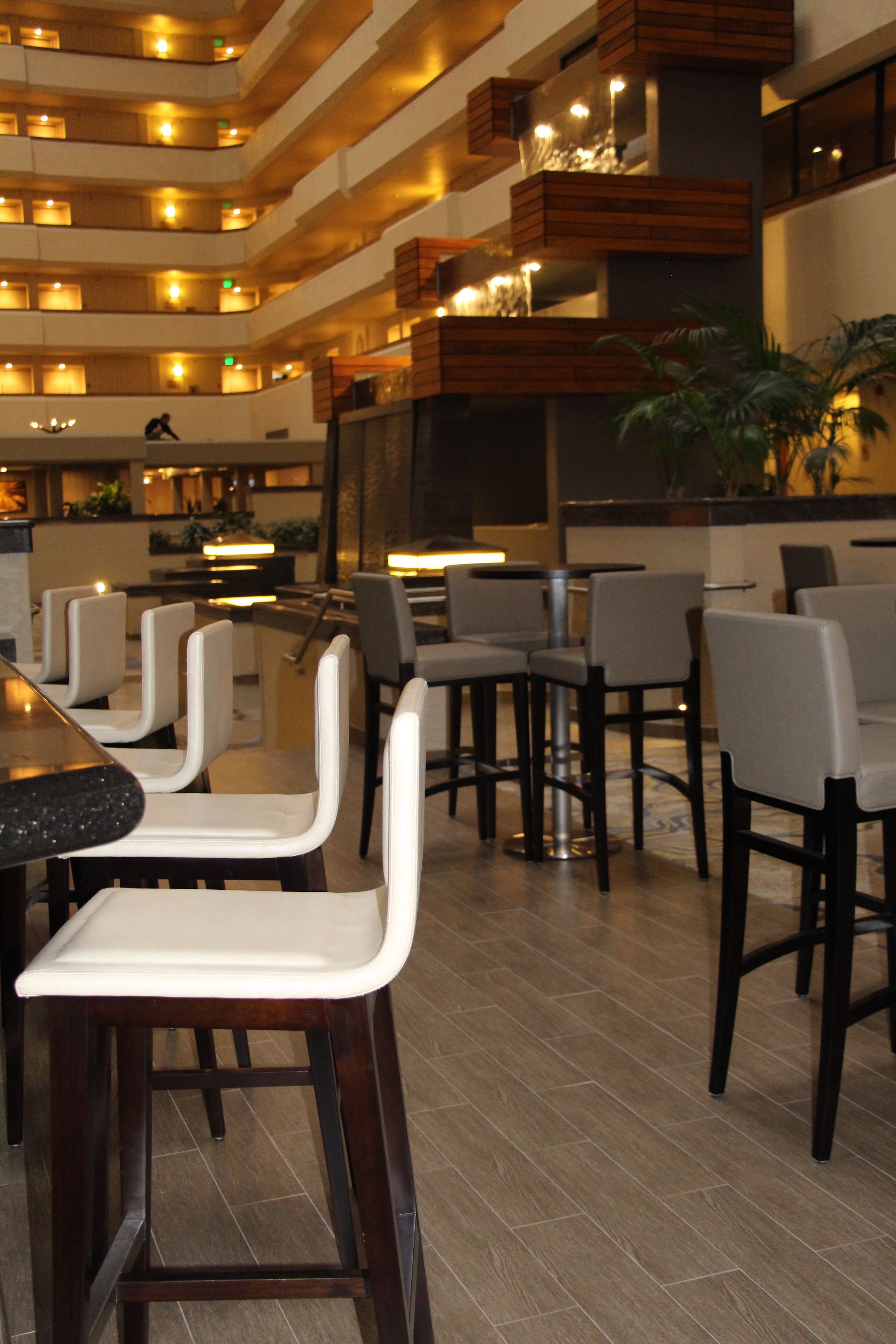 Un moderno vestíbulo de hotel con varias zonas de restauración, detalles de madera y un bar central.