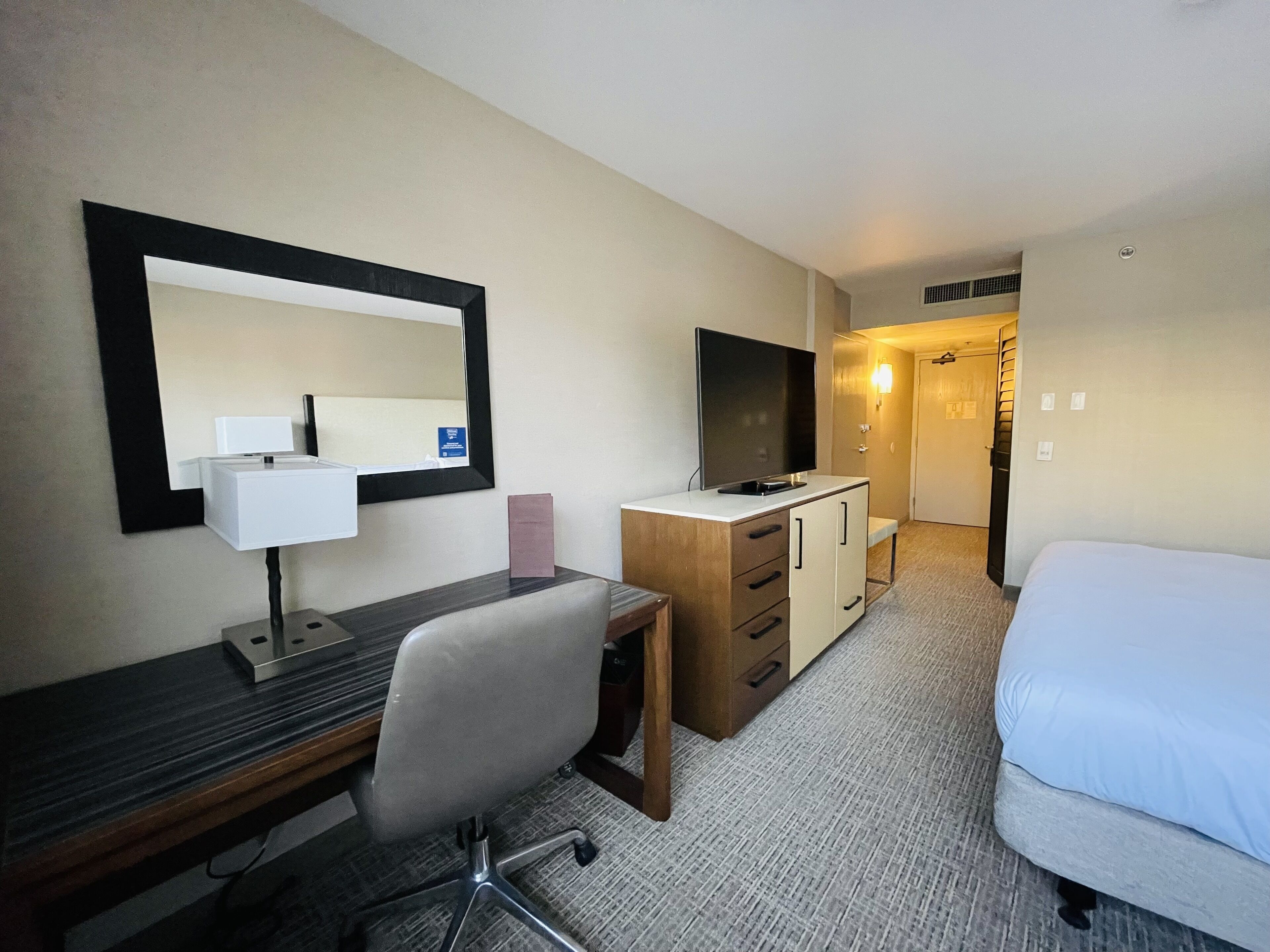 Ein Hotelzimmer mit Schreibtisch, Stuhl, Fernseher, Kleiderschrank und einem Bett.