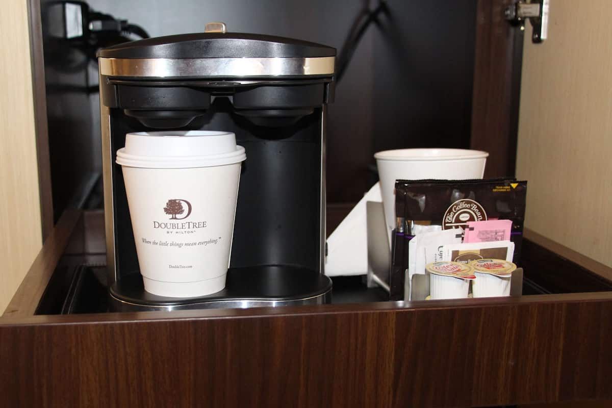 A coffee maker, a disposable cup, and coffee pods in a hotel room's minibar.