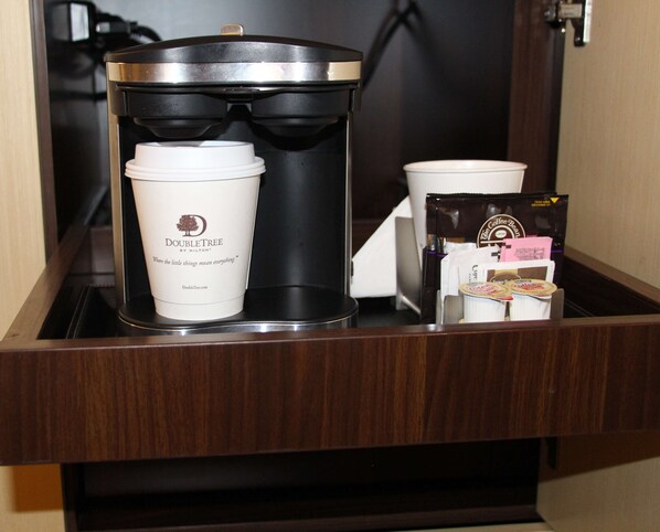 A coffee maker, a disposable cup, and coffee pods in a hotel room's minibar.