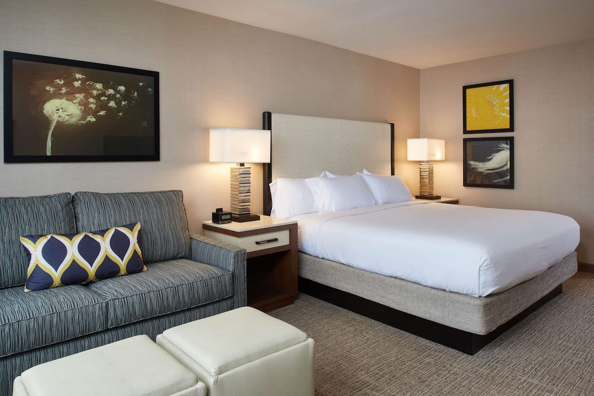 A hotel room with a bed, a sofa, a nightstand, and a lamp.
